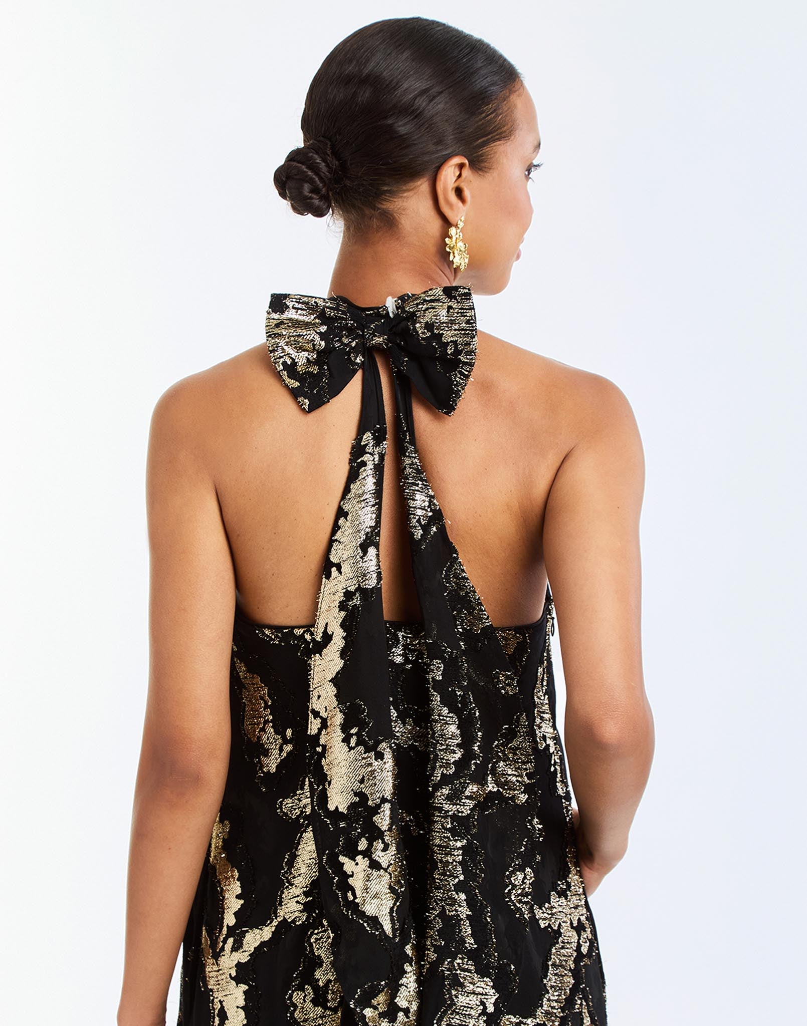 Adelina Gown in Black/Gold detail – metallic jacquard evening gown with halter bow neckline, faux ruffle back, A-line silhouette, and side seam pockets by Mestiza New York.