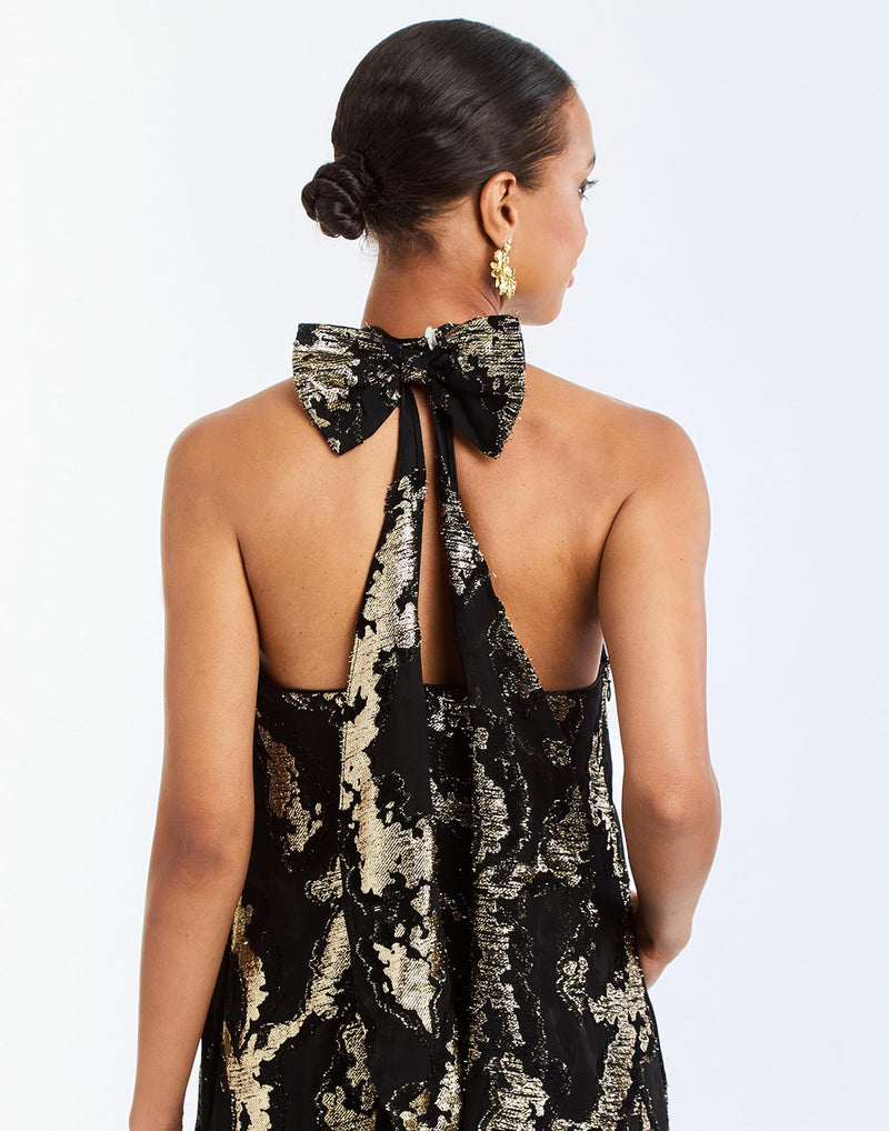 Adelina Gown in Black/Gold detail – metallic jacquard evening gown with halter bow neckline, faux ruffle back, A-line silhouette, and side seam pockets by Mestiza New York.