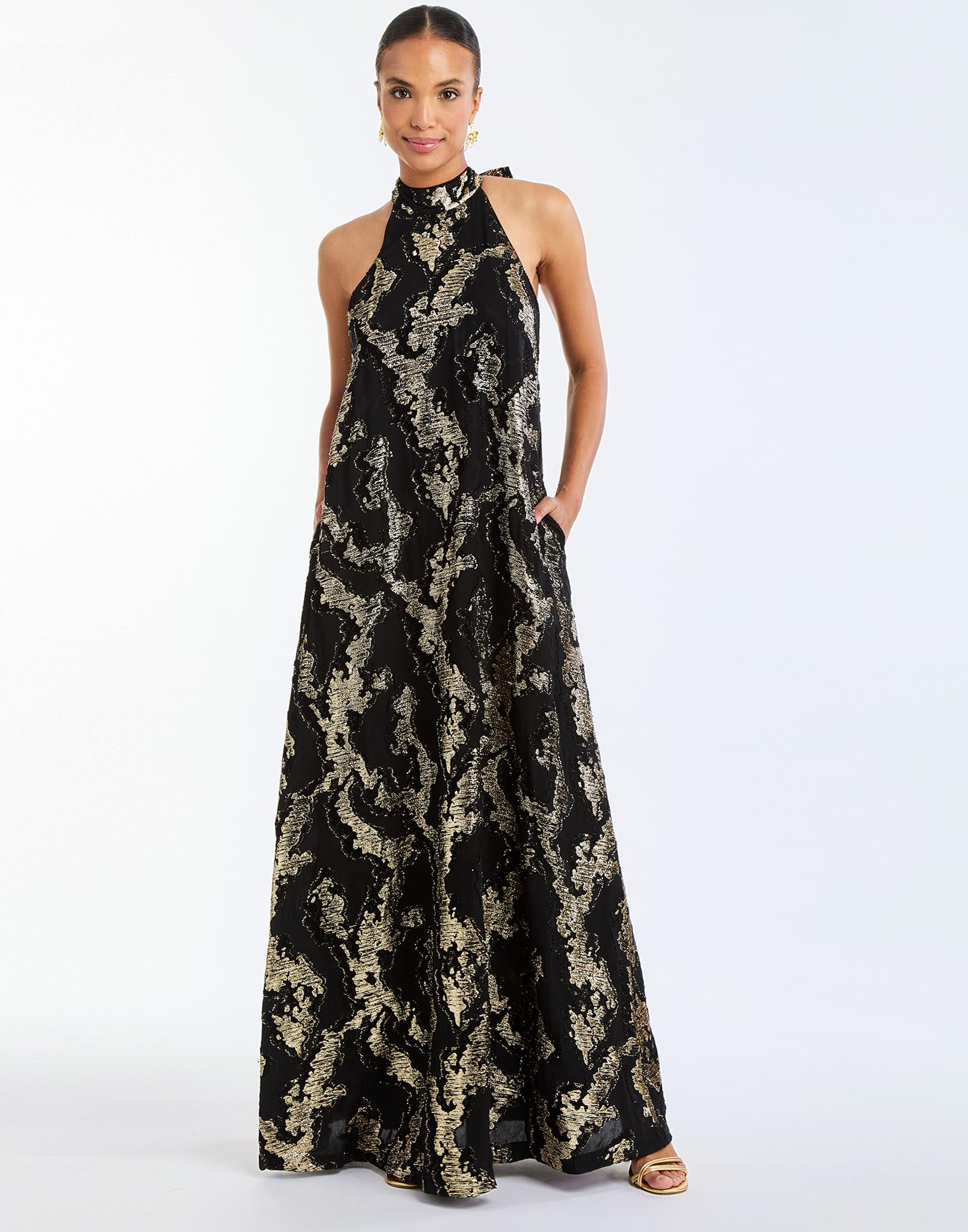 Adelina Gown in Black/Gold front – metallic jacquard evening gown with halter bow neckline, faux ruffle back, A-line silhouette, and side seam pockets by Mestiza New York.