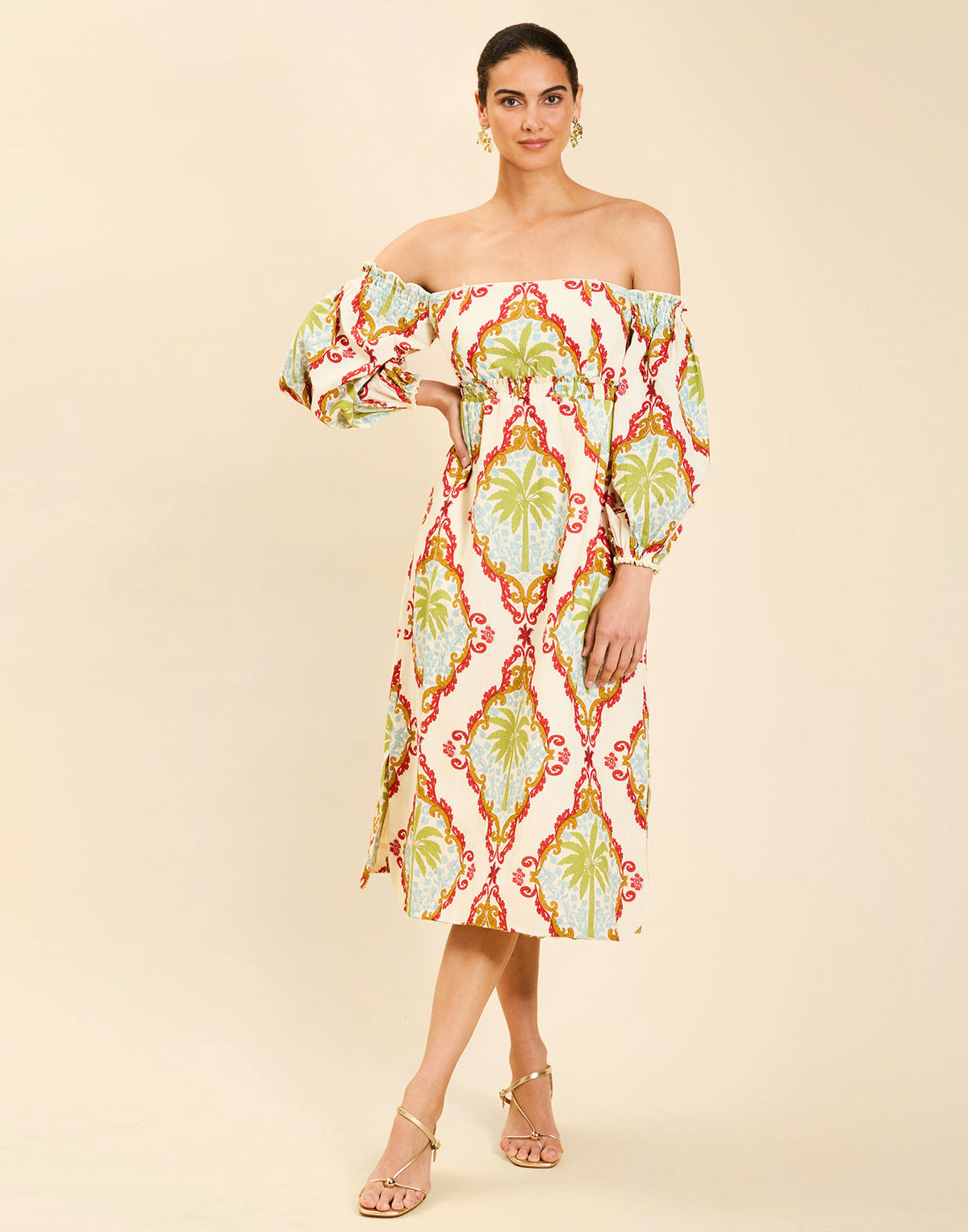 Woman wearing the Mestiza Benny Midi Dress in Mediterranean Sage print, featuring an off-the-shoulder neckline, empire waist, balloon sleeves, A-line skirt, and breathable linen fabrication.