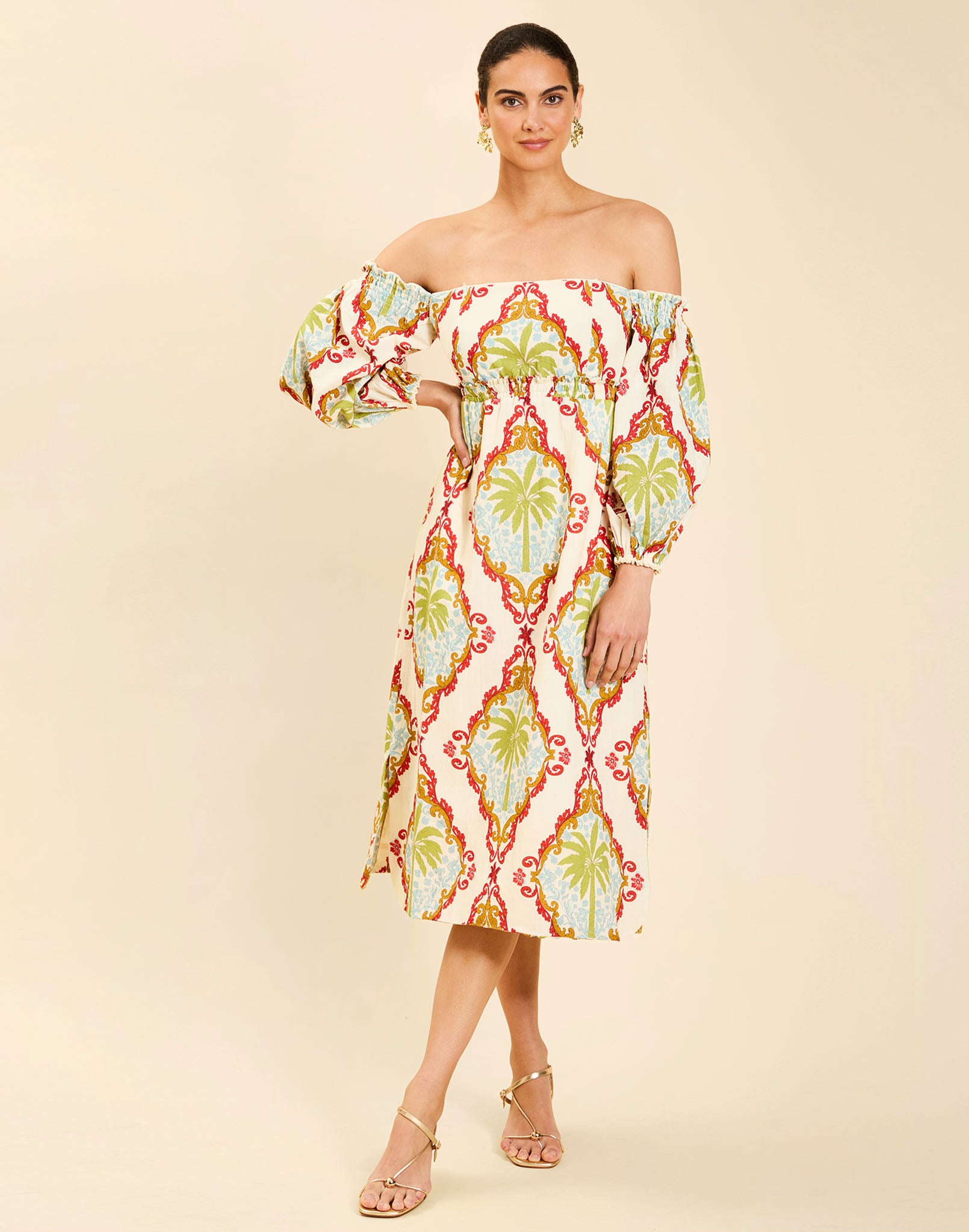 Woman wearing the Mestiza Benny Midi Dress in Mediterranean Sage print, featuring an off-the-shoulder neckline, empire waist, balloon sleeves, A-line skirt, and breathable linen fabrication.