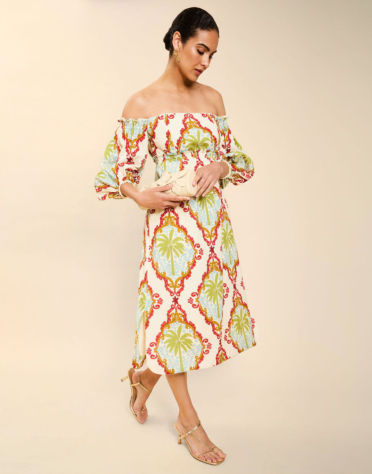 Woman wearing the Mestiza Benny Midi Dress in Mediterranean Sage print, featuring an off-the-shoulder neckline, empire waist, balloon sleeves, A-line skirt, and breathable linen fabrication.