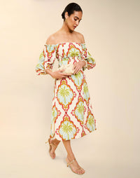 Woman wearing the Mestiza Benny Midi Dress in Mediterranean Sage print, featuring an off-the-shoulder neckline, empire waist, balloon sleeves, A-line skirt, and breathable linen fabrication.