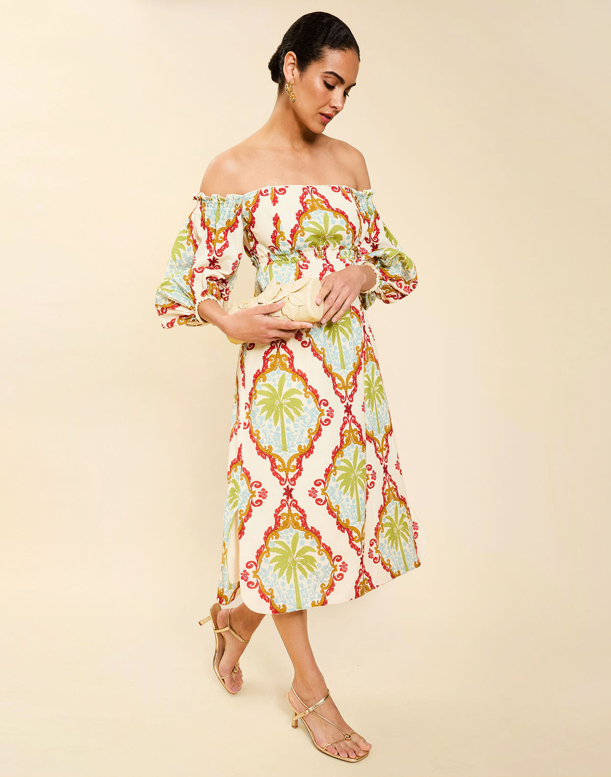 Woman wearing the Mestiza Benny Midi Dress in Mediterranean Sage print, featuring an off-the-shoulder neckline, empire waist, balloon sleeves, A-line skirt, and breathable linen fabrication.