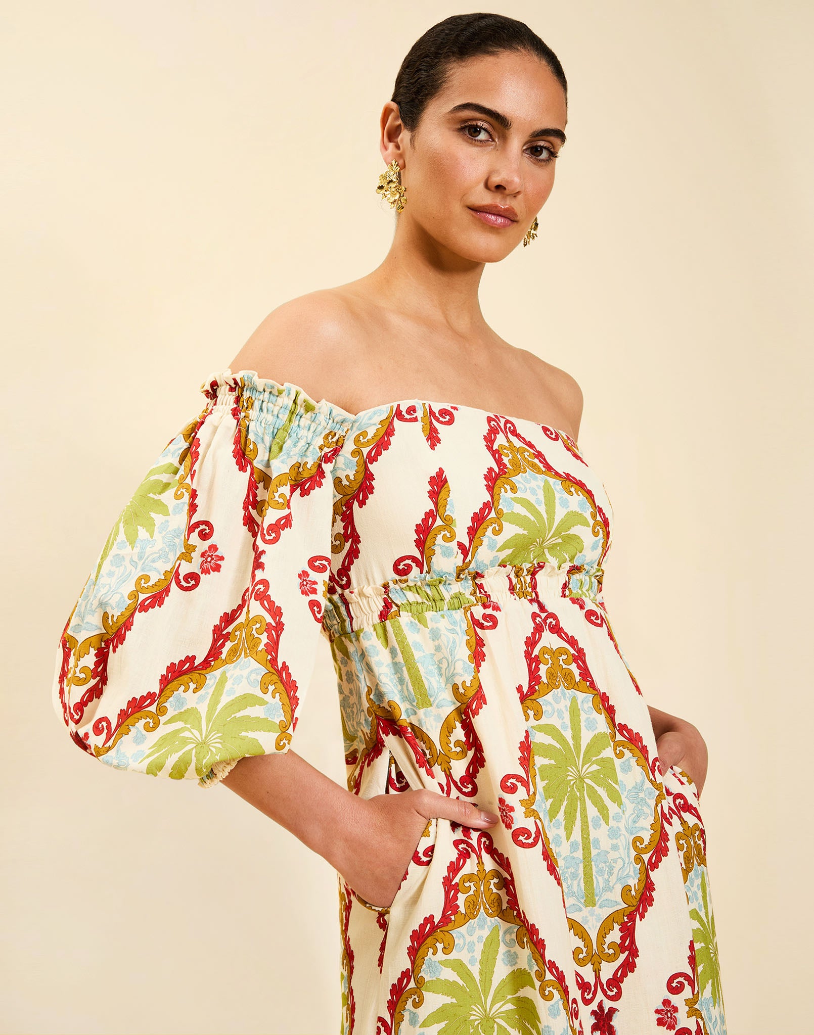 Woman wearing the Mestiza Benny Midi Dress in Mediterranean Sage print, featuring an off-the-shoulder neckline, empire waist, balloon sleeves, A-line skirt, and breathable linen fabrication.
