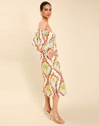 Woman wearing the Mestiza Benny Midi Dress in Mediterranean Sage print, featuring an off-the-shoulder neckline, empire waist, balloon sleeves, A-line skirt, and breathable linen fabrication.