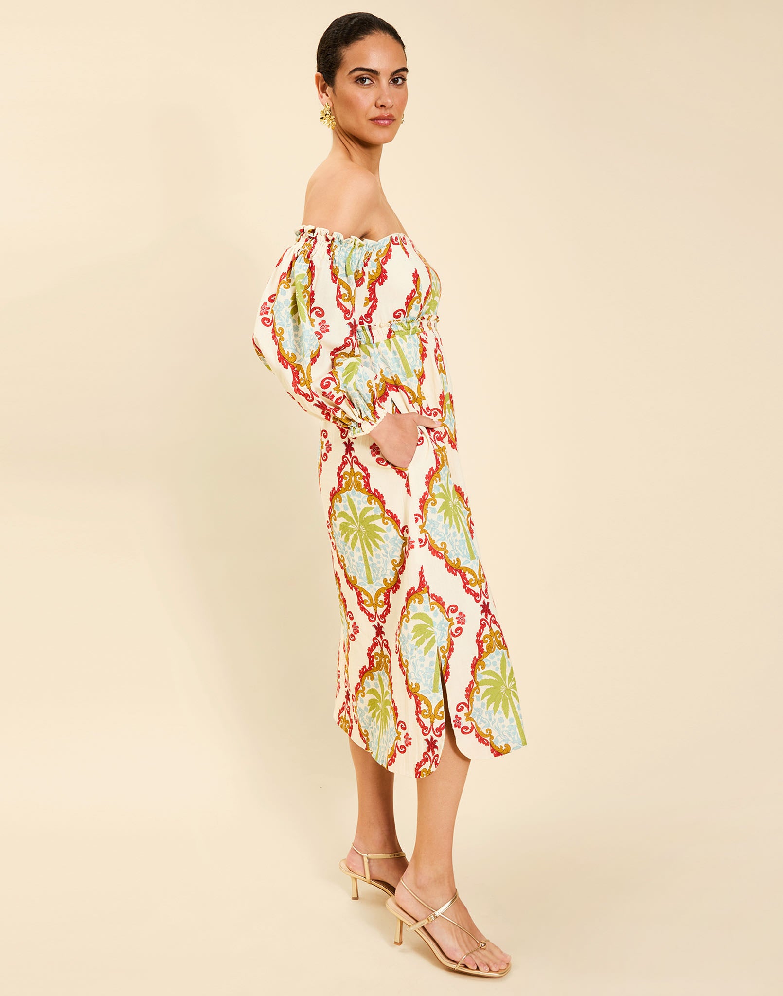 Woman wearing the Mestiza Benny Midi Dress in Mediterranean Sage print, featuring an off-the-shoulder neckline, empire waist, balloon sleeves, A-line skirt, and breathable linen fabrication.