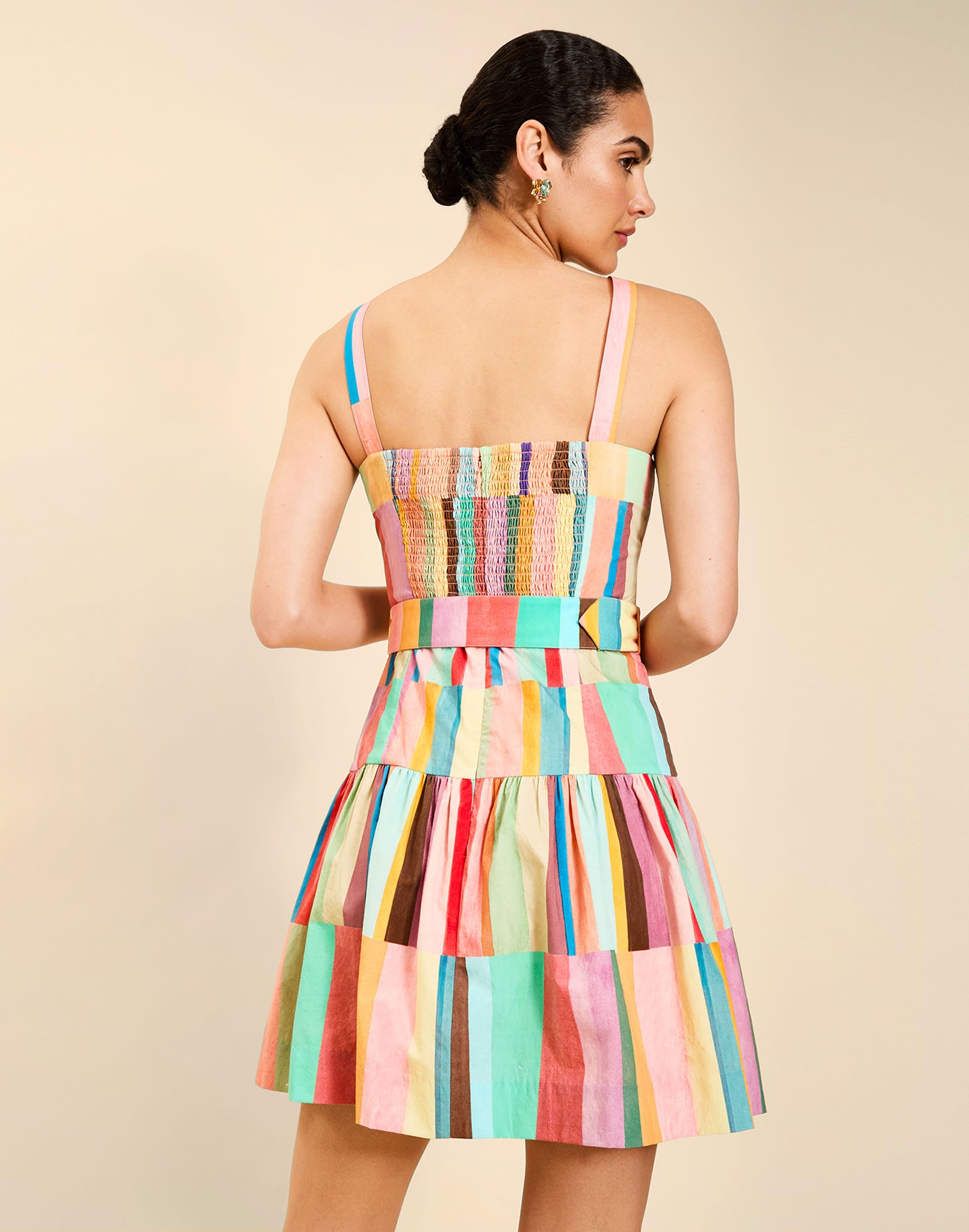 Woman wearing the Mestiza Castellano Mini Dress in Southwest Sunset print, featuring a drop-waist silhouette, fitted bodice with princess seams, adjustable straps, gathered skirt, coordinating belt, and cotton poplin fabrication.