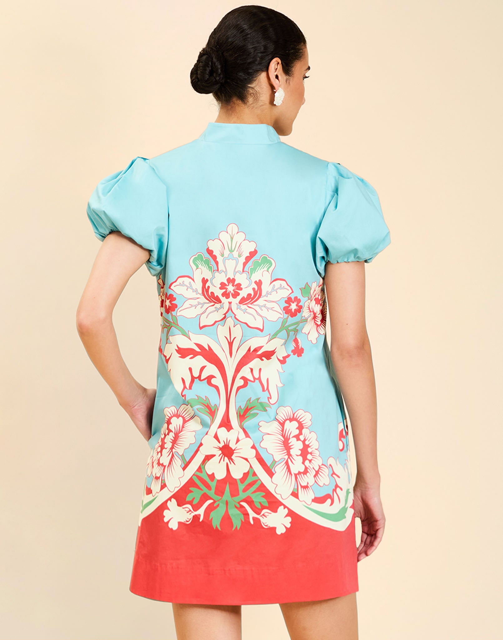 Woman wearing the Mestiza Elliana Mini Dress in La Botanica Blue print, featuring an A-line silhouette, mandarin collar, V-neckline, pleated puff sleeves, and cotton poplin fabrication.