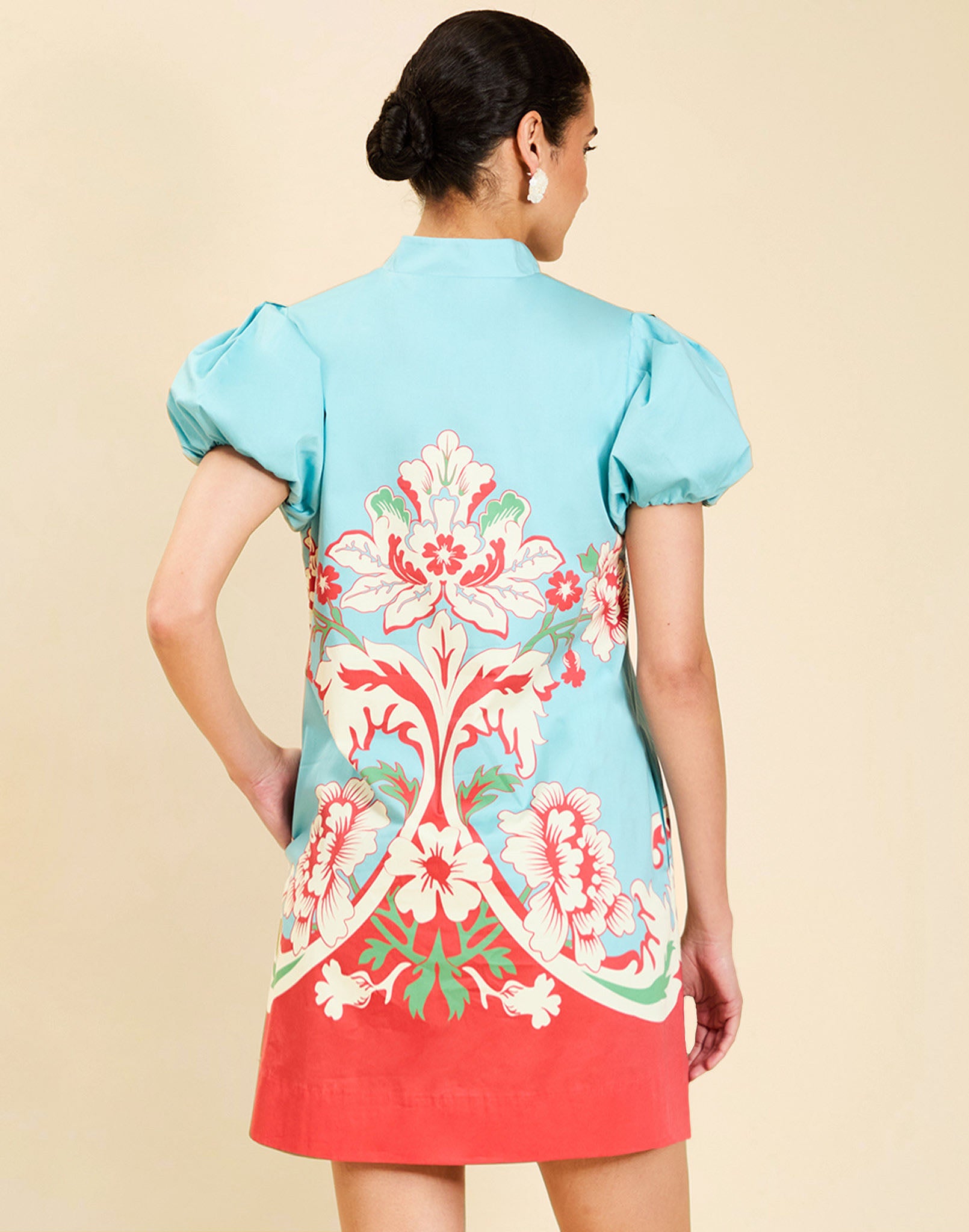 Woman wearing the Mestiza Elliana Mini Dress in La Botanica Blue print, featuring an A-line silhouette, mandarin collar, V-neckline, pleated puff sleeves, and cotton poplin fabrication.