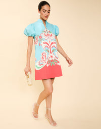 Woman wearing the Mestiza Elliana Mini Dress in La Botanica Blue print, featuring an A-line silhouette, mandarin collar, V-neckline, pleated puff sleeves, and cotton poplin fabrication.