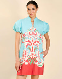 Woman wearing the Mestiza Elliana Mini Dress in La Botanica Blue print, featuring an A-line silhouette, mandarin collar, V-neckline, pleated puff sleeves, and cotton poplin fabrication.