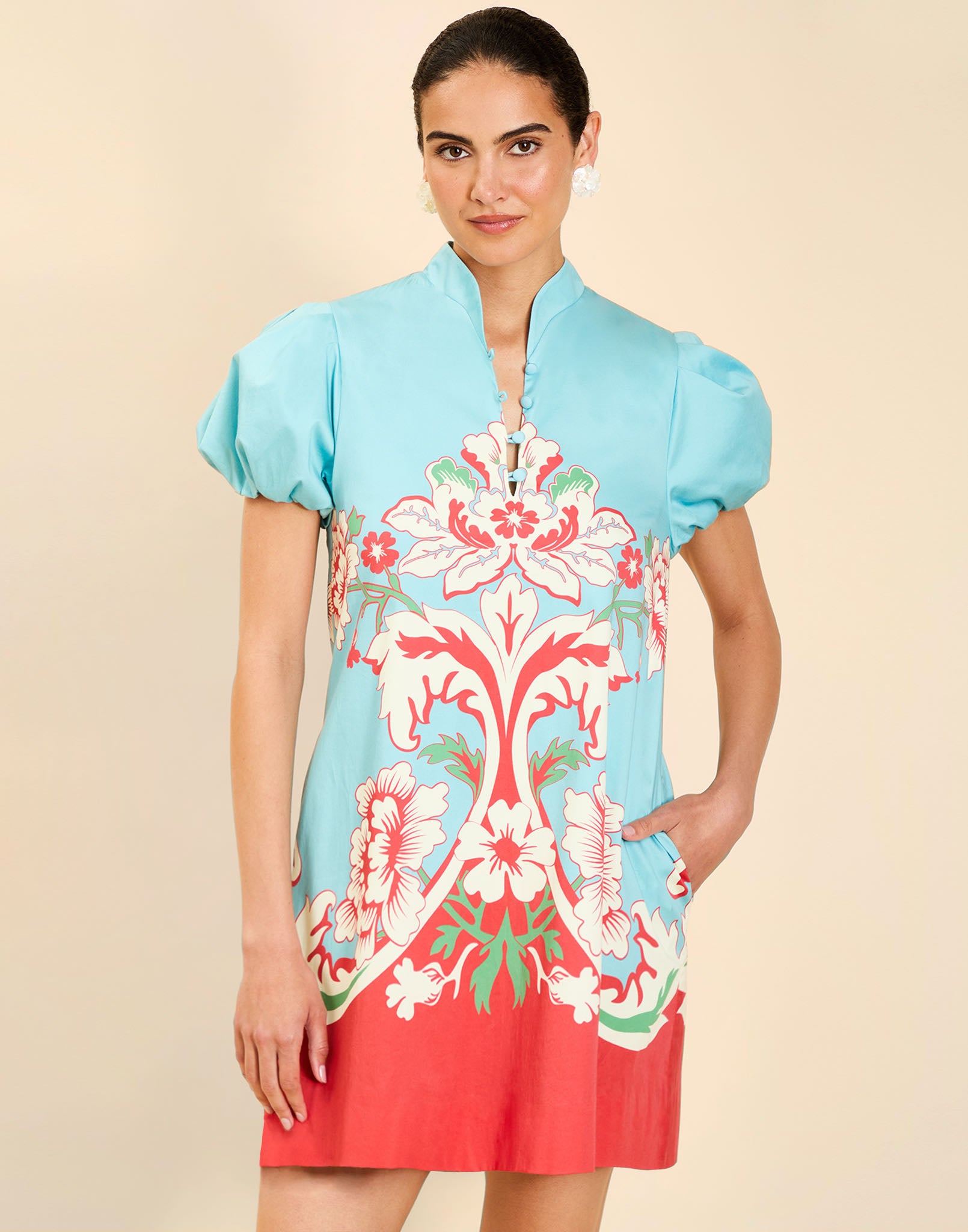 Woman wearing the Mestiza Elliana Mini Dress in La Botanica Blue print, featuring an A-line silhouette, mandarin collar, V-neckline, pleated puff sleeves, and cotton poplin fabrication.