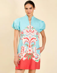 Woman wearing the Mestiza Elliana Mini Dress in La Botanica Blue print, featuring an A-line silhouette, mandarin collar, V-neckline, pleated puff sleeves, and cotton poplin fabrication.