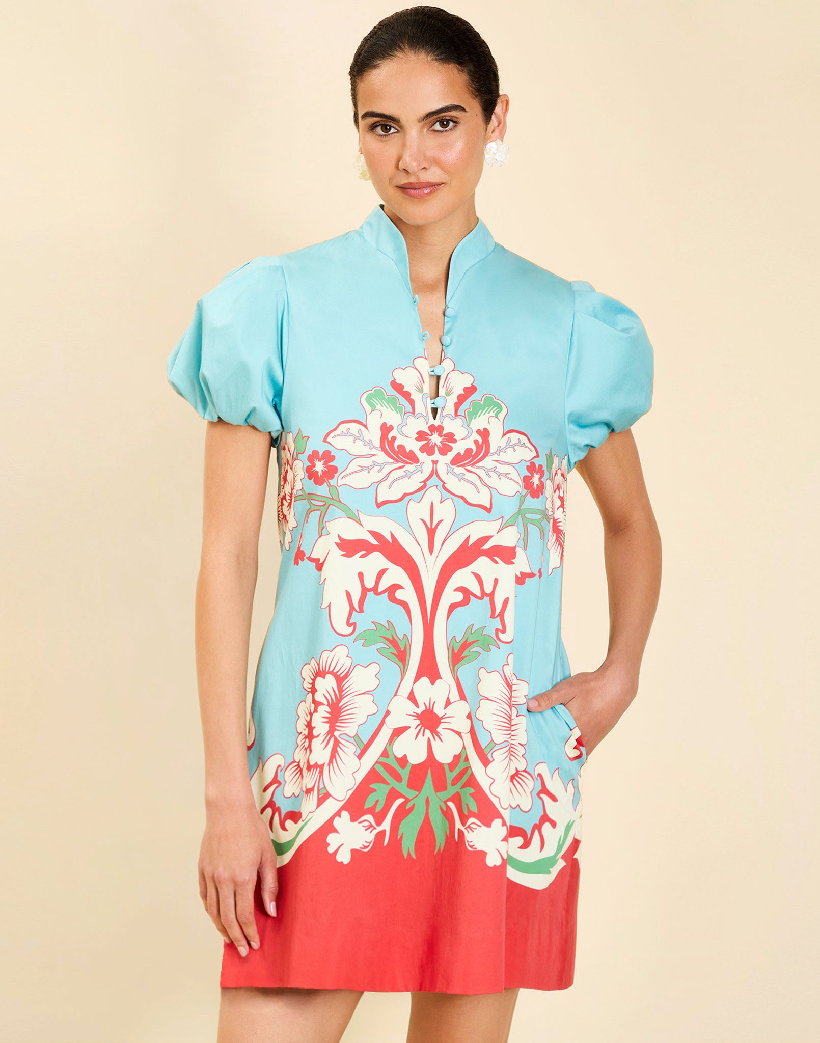 Woman wearing the Mestiza Elliana Mini Dress in La Botanica Blue print, featuring an A-line silhouette, mandarin collar, V-neckline, pleated puff sleeves, and cotton poplin fabrication.