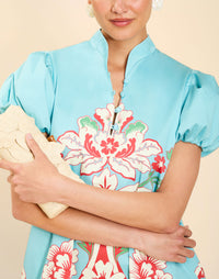 Woman wearing the Mestiza Elliana Mini Dress in La Botanica Blue print, featuring an A-line silhouette, mandarin collar, V-neckline, pleated puff sleeves, and cotton poplin fabrication.