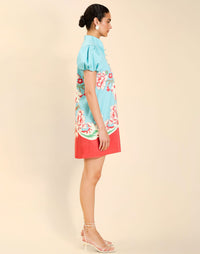 Woman wearing the Mestiza Elliana Mini Dress in La Botanica Blue print, featuring an A-line silhouette, mandarin collar, V-neckline, pleated puff sleeves, and cotton poplin fabrication.
