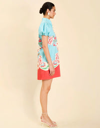 Woman wearing the Mestiza Elliana Mini Dress in La Botanica Blue print, featuring an A-line silhouette, mandarin collar, V-neckline, pleated puff sleeves, and cotton poplin fabrication.