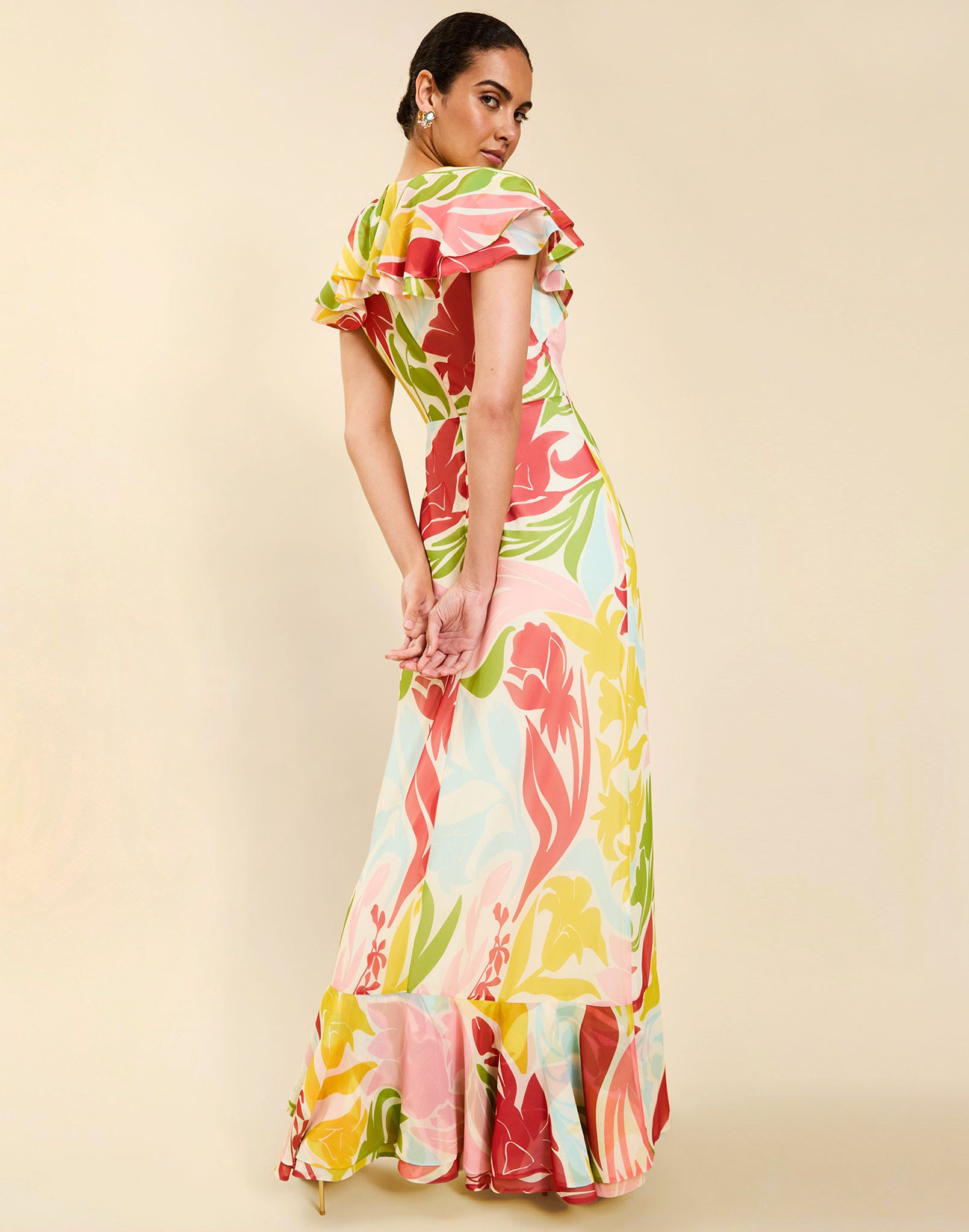 Woman wearing the Mestiza Fernanda Gown in Autumn Daydreaming print, featuring a V-neckline, cascading ruffle details, cap-style ruffle sleeves, fitted bodice, and flowing chiffon skirt.