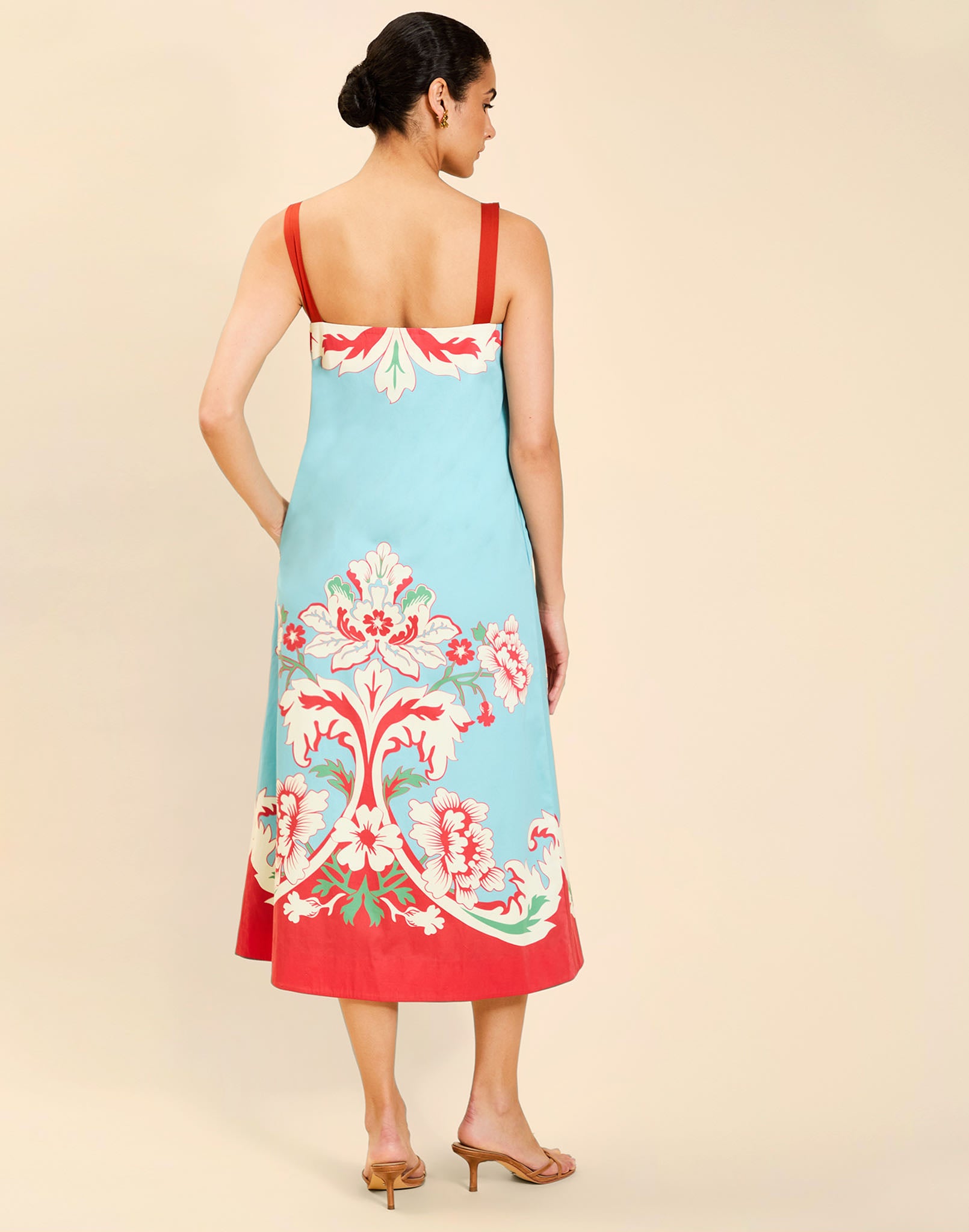 Woman wearing the Mestiza Galena Tea Length Dress in La Botanica Blue print, featuring a column silhouette, straight-across neckline, adjustable straps, side seam pockets, and cotton poplin fabrication.