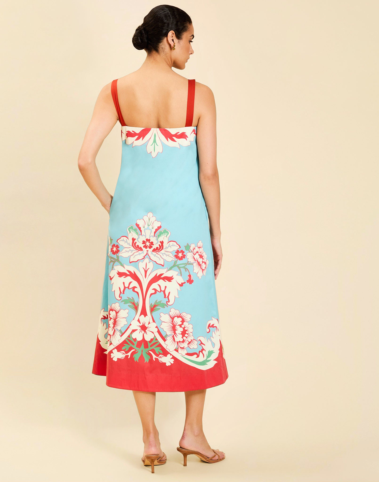 Woman wearing the Mestiza Galena Tea Length Dress in La Botanica Blue print, featuring a column silhouette, straight-across neckline, adjustable straps, side seam pockets, and cotton poplin fabrication.