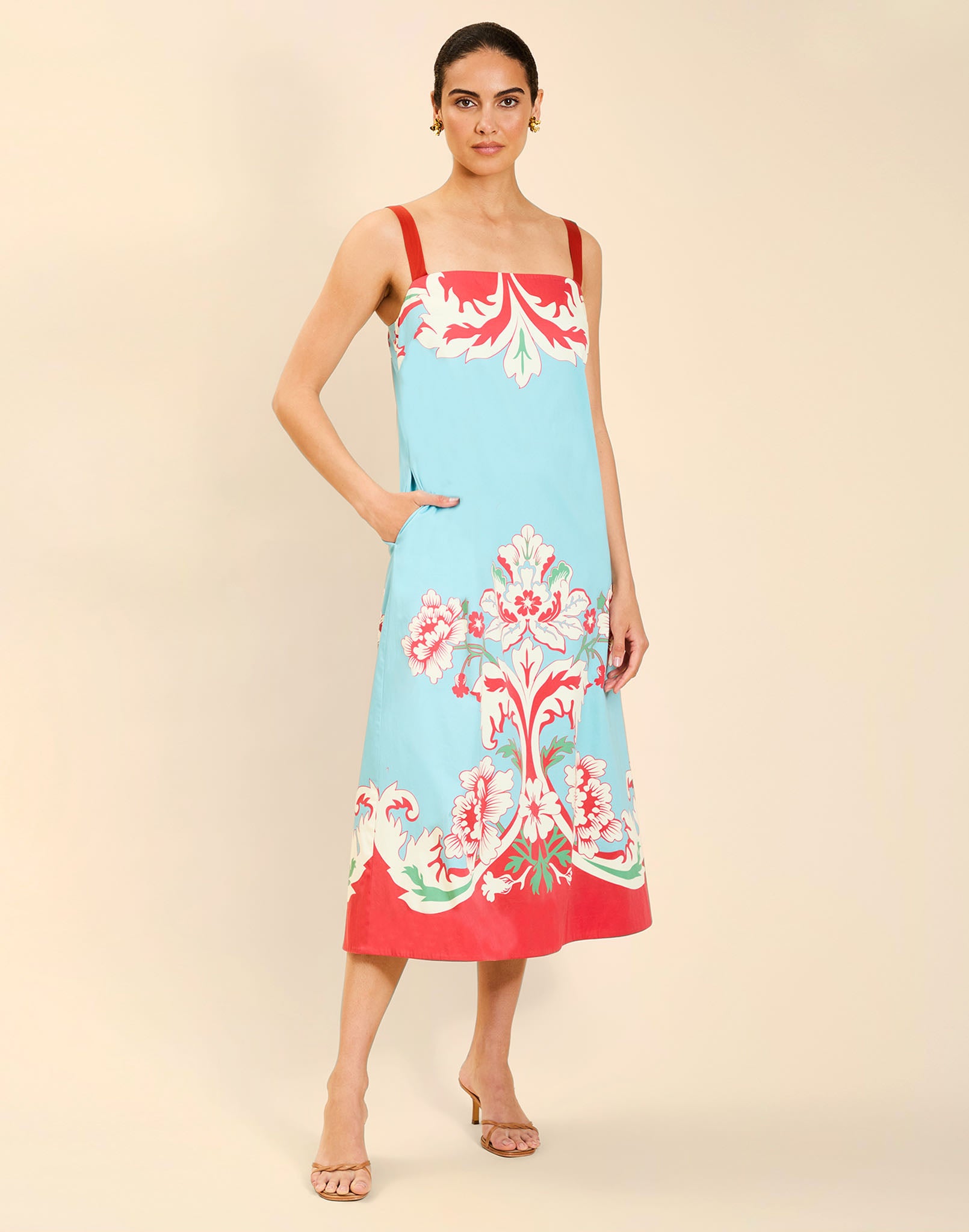 Woman wearing the Mestiza Galena Tea Length Dress in La Botanica Blue print, featuring a column silhouette, straight-across neckline, adjustable straps, side seam pockets, and cotton poplin fabrication.