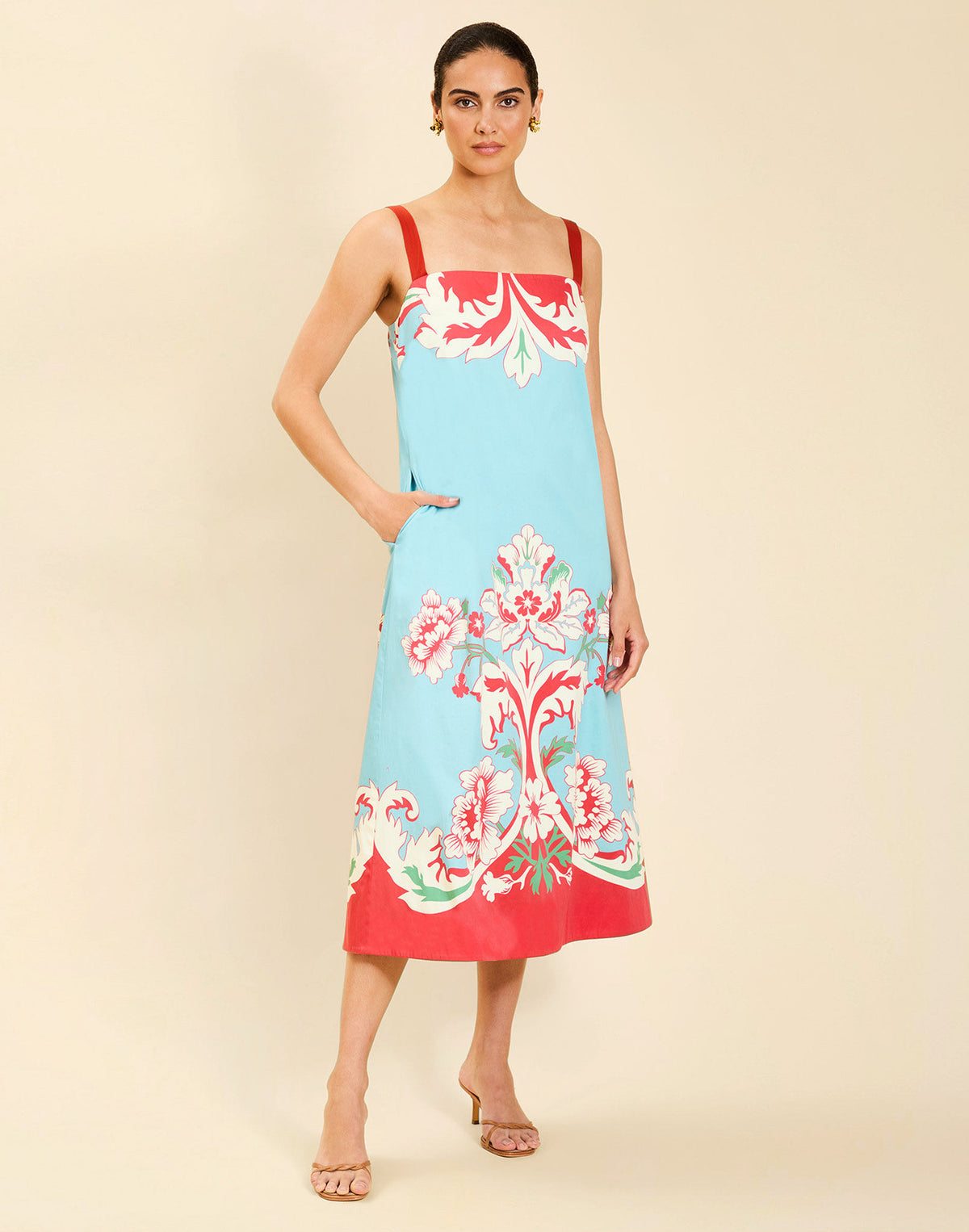 Woman wearing the Mestiza Galena Tea Length Dress in La Botanica Blue print, featuring a column silhouette, straight-across neckline, adjustable straps, side seam pockets, and cotton poplin fabrication.