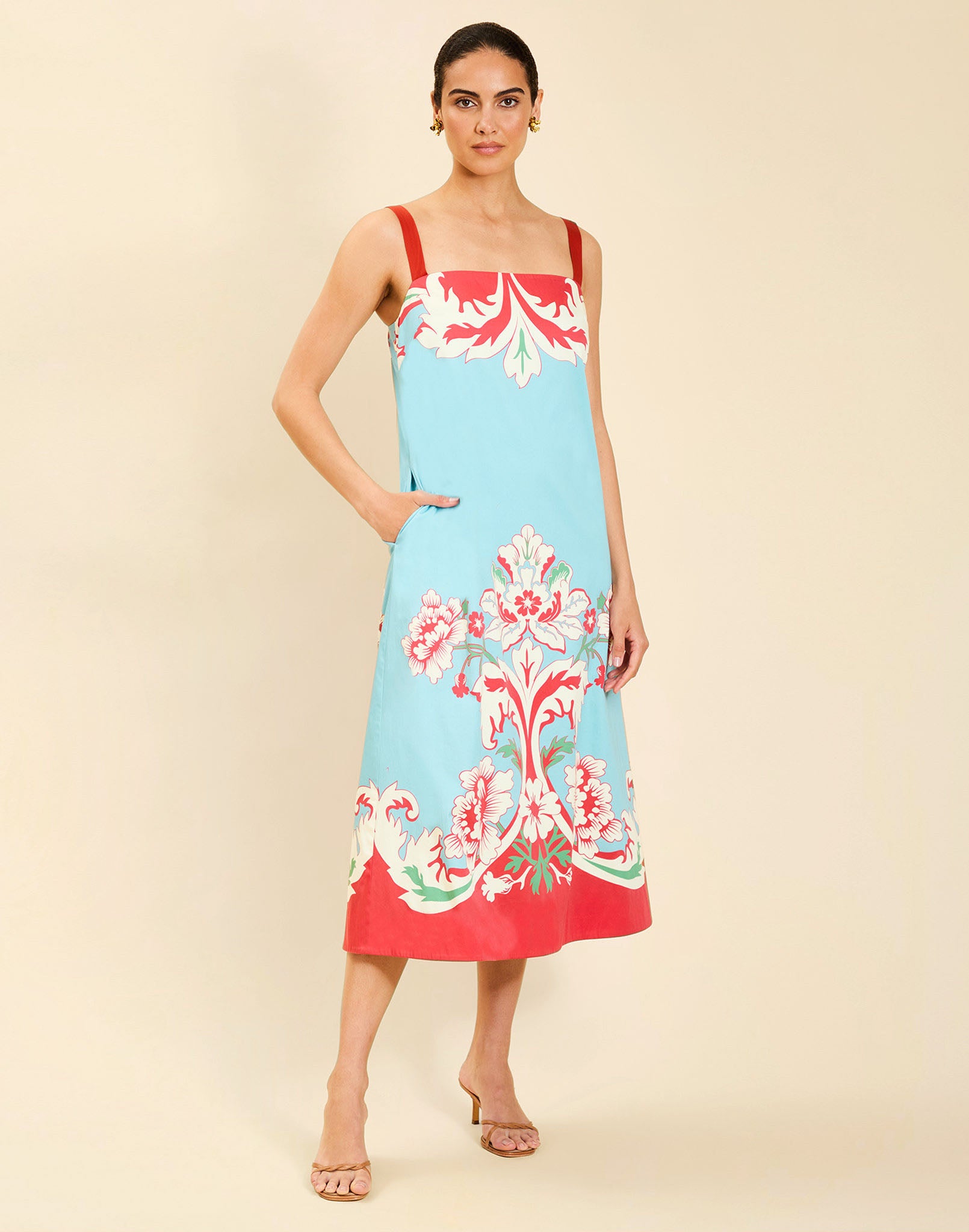 Woman wearing the Mestiza Galena Tea Length Dress in La Botanica Blue print, featuring a column silhouette, straight-across neckline, adjustable straps, side seam pockets, and cotton poplin fabrication.