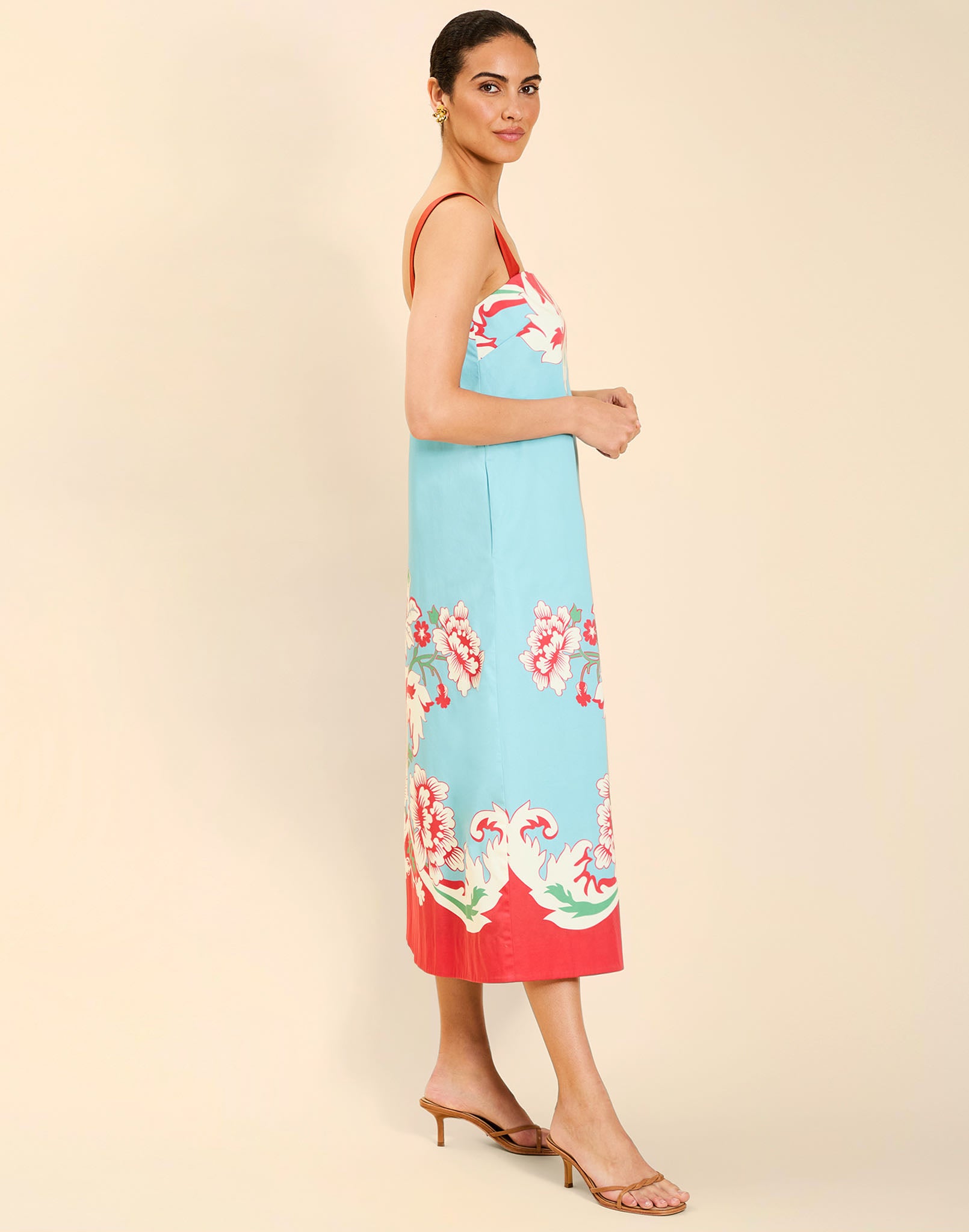 Woman wearing the Mestiza Galena Tea Length Dress in La Botanica Blue print, featuring a column silhouette, straight-across neckline, adjustable straps, side seam pockets, and cotton poplin fabrication.