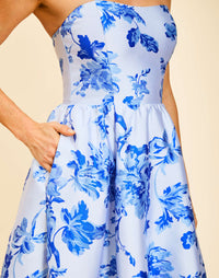 Strapless gown in Porcelain Blue Jacquard featuring a fitted bodice, cascading asymmetrical skirt, removable straps, and functional pockets.