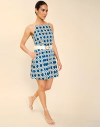 Woman wearing the Mestiza Havana Mini Dress in Solihiya Navy print, featuring a bib-neckline, bell skirt, removable belt, princess seaming, side seam pockets, and cotton poplin fabrication.