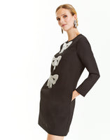 Black mini shift dress with sleeves, pockets, and sequined bow embellishments on front. 