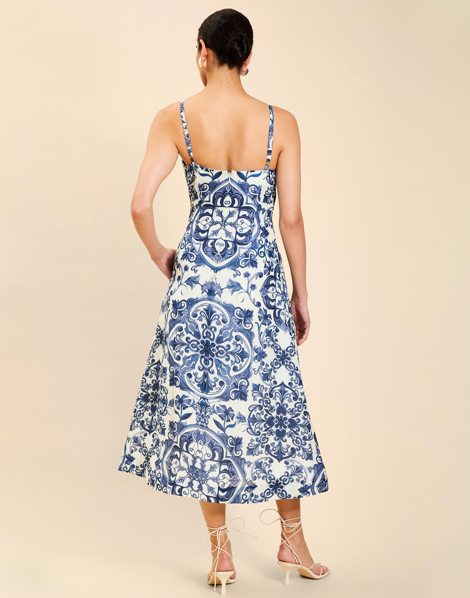 Woman wearing the Mestiza Ladera Midi Dress in Azulejo Navy print, featuring a fitted bodice, full A-line skirt, straight-across neckline, adjustable straps, side seam pockets, and linen organza fabrication.