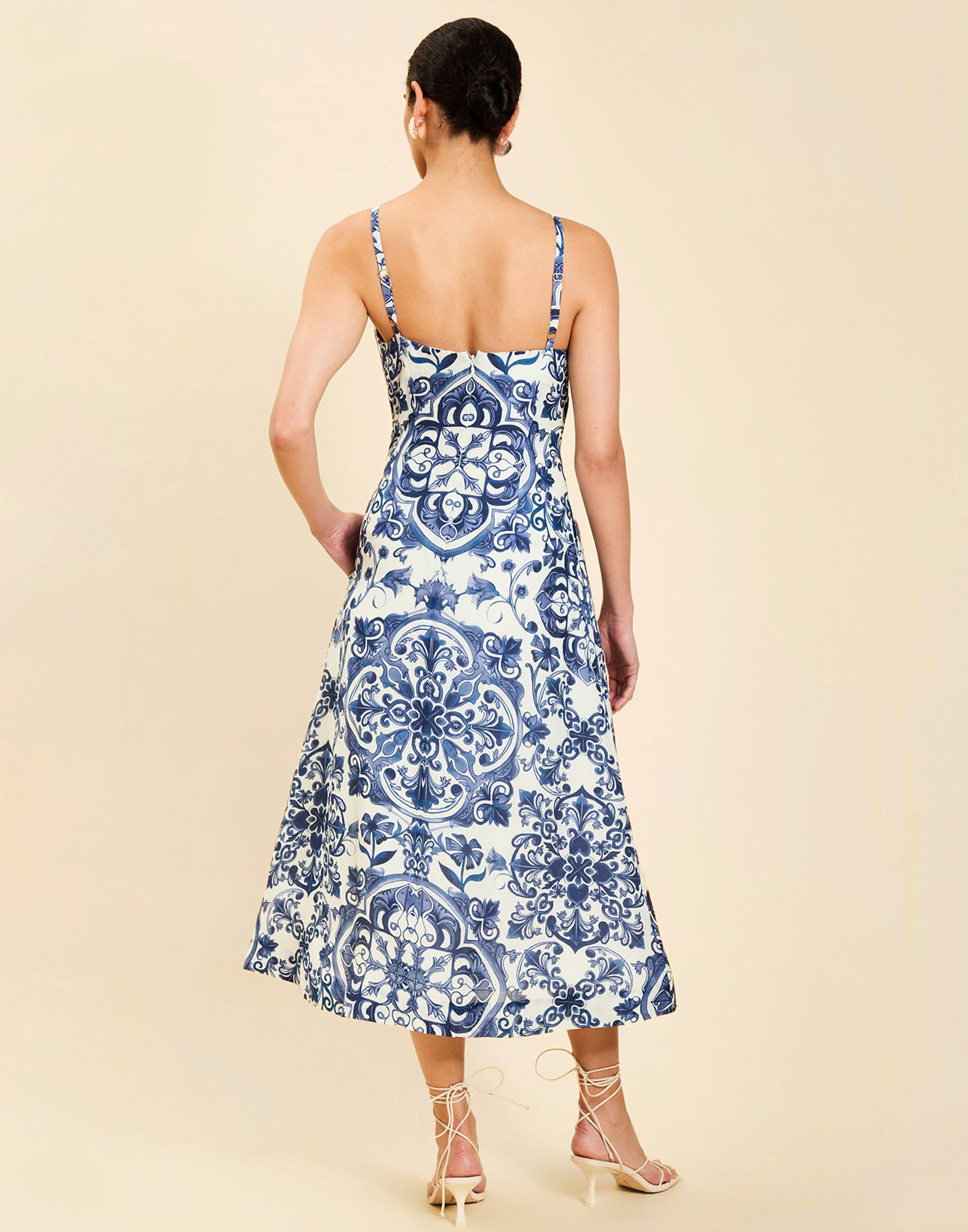 Woman wearing the Mestiza Ladera Midi Dress in Azulejo Navy print, featuring a fitted bodice, full A-line skirt, straight-across neckline, adjustable straps, side seam pockets, and linen organza fabrication.