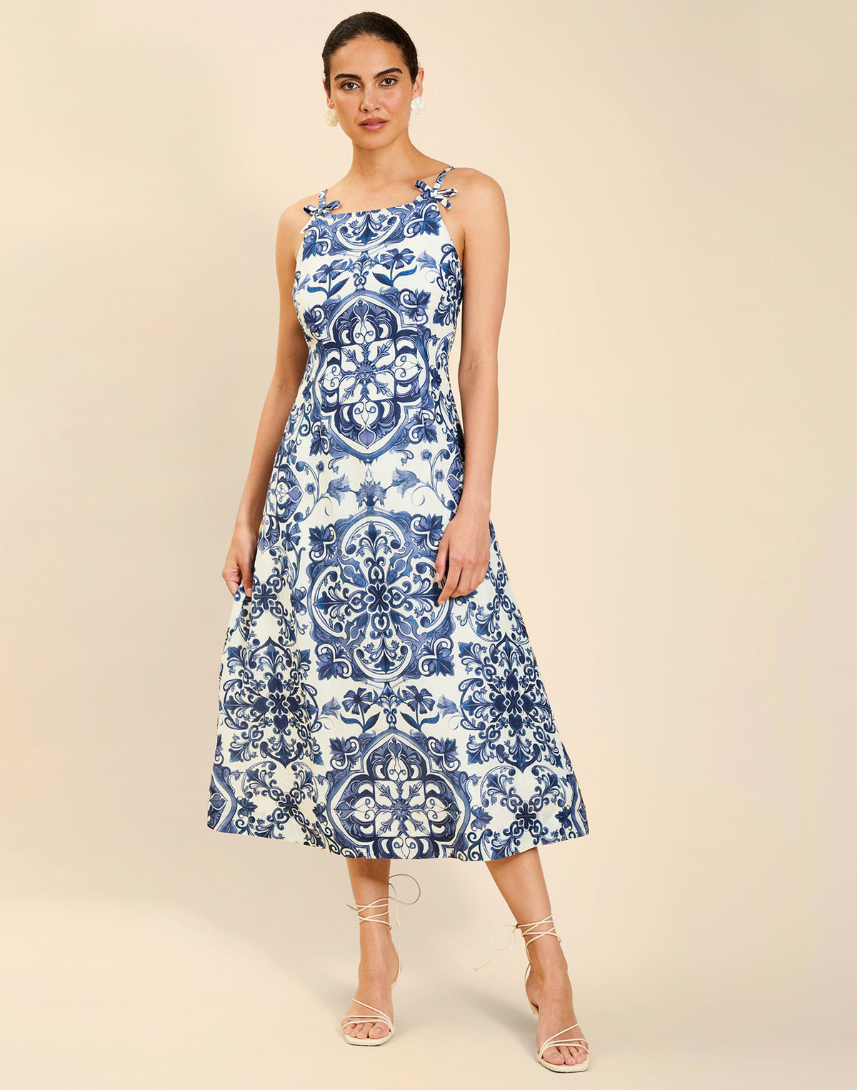 Woman wearing the Mestiza Ladera Midi Dress in Azulejo Navy print, featuring a fitted bodice, full A-line skirt, straight-across neckline, adjustable straps, side seam pockets, and linen organza fabrication.