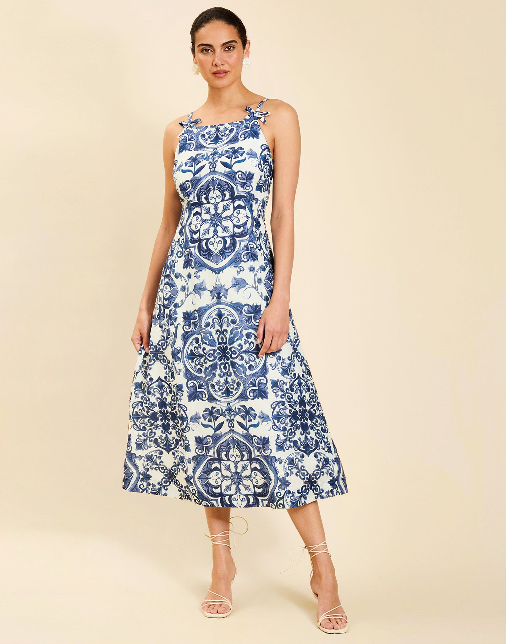 Woman wearing the Mestiza Ladera Midi Dress in Azulejo Navy print, featuring a fitted bodice, full A-line skirt, straight-across neckline, adjustable straps, side seam pockets, and linen organza fabrication.
