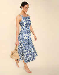 Woman wearing the Mestiza Ladera Midi Dress in Azulejo Navy print, featuring a fitted bodice, full A-line skirt, straight-across neckline, adjustable straps, side seam pockets, and linen organza fabrication.