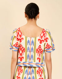Woman wearing the Mestiza Maldives Top in Ikat Sunrise print, featuring a boxy silhouette, deep scoop neckline, pleated flutter sleeves, contrast ivory trim, and lightweight linen fabrication.