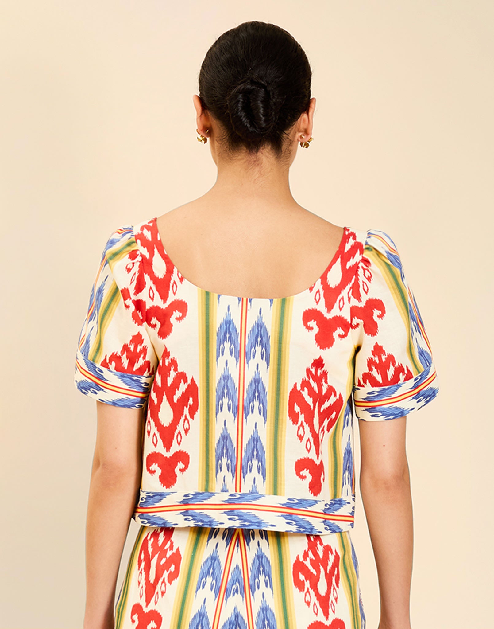 Woman wearing the Mestiza Maldives Top in Ikat Sunrise print, featuring a boxy silhouette, deep scoop neckline, pleated flutter sleeves, contrast ivory trim, and lightweight linen fabrication.