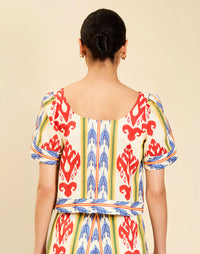 Woman wearing the Mestiza Maldives Top in Ikat Sunrise print, featuring a boxy silhouette, deep scoop neckline, pleated flutter sleeves, contrast ivory trim, and lightweight linen fabrication.