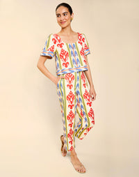 Woman wearing the Mestiza Maldives Top in Ikat Sunrise print, featuring a boxy silhouette, deep scoop neckline, pleated flutter sleeves, contrast ivory trim, and lightweight linen fabrication.