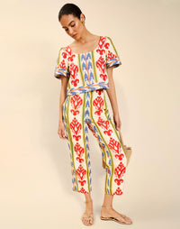 Woman wearing the Mestiza Palau Cigarette Pant in Ikat Sunrise print, featuring a slim-fit cigarette silhouette, front pleat detailing, cropped ankle-length fit, and lightweight linen fabrication.