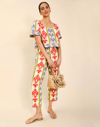 Woman wearing the Mestiza Maldives Top in Ikat Sunrise print, featuring a boxy silhouette, deep scoop neckline, pleated flutter sleeves, contrast ivory trim, and lightweight linen fabrication.