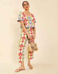 Woman wearing the Mestiza Maldives Top in Ikat Sunrise print, featuring a boxy silhouette, deep scoop neckline, pleated flutter sleeves, contrast ivory trim, and lightweight linen fabrication.