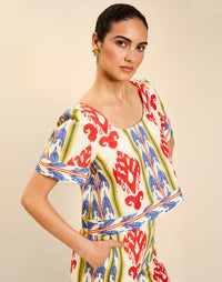 Woman wearing the Mestiza Maldives Top in Ikat Sunrise print, featuring a boxy silhouette, deep scoop neckline, pleated flutter sleeves, contrast ivory trim, and lightweight linen fabrication.