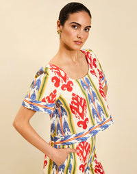 Woman wearing the Mestiza Maldives Top in Ikat Sunrise print, featuring a boxy silhouette, deep scoop neckline, pleated flutter sleeves, contrast ivory trim, and lightweight linen fabrication.