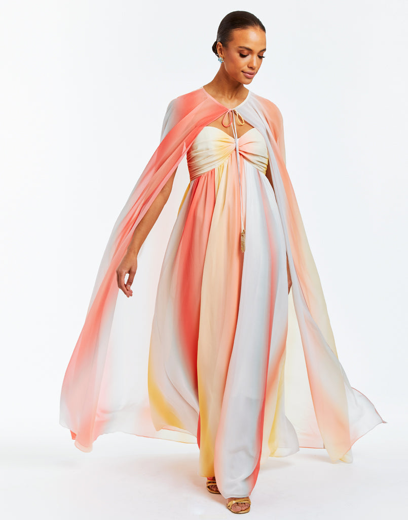 Floor length chiffon evening gown with vertical ombre in sunset colors, featuring a sweetheart neckline, ruched bodice and a full length removable cape. 
