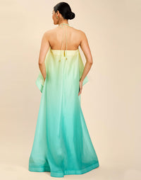 Woman wearing the Mestiza Mariposa Convertible Gown in Tuscan Sunrise print, featuring a column silhouette, removable cape overlay, racerback neckline, open back, self-tie halter straps, and linen organza fabrication.