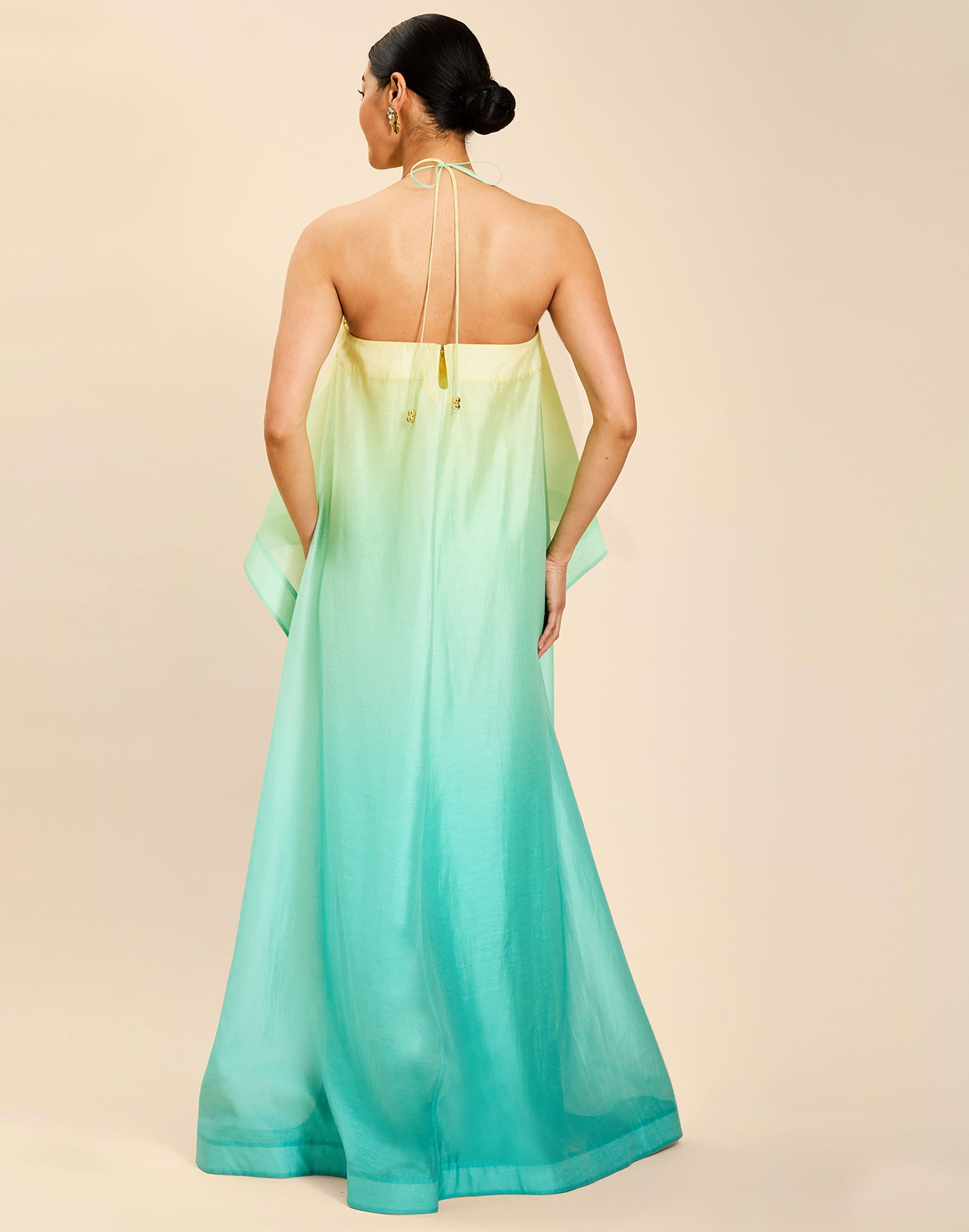 Woman wearing the Mestiza Mariposa Convertible Gown in Tuscan Sunrise print, featuring a column silhouette, removable cape overlay, racerback neckline, open back, self-tie halter straps, and linen organza fabrication.