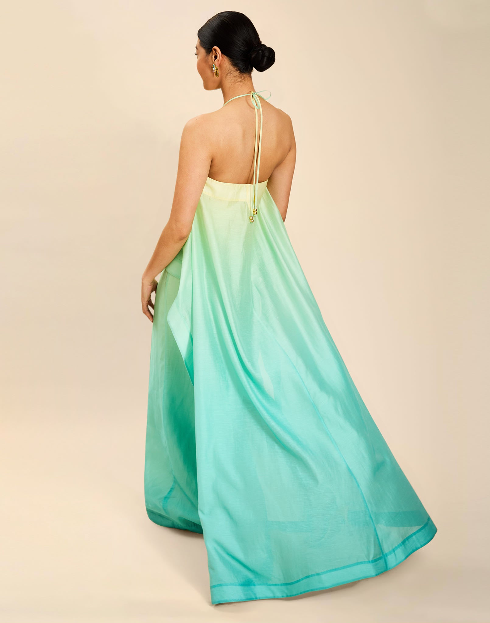 Woman wearing the Mestiza Mariposa Convertible Gown in Tuscan Sunrise print, featuring a column silhouette, removable cape overlay, racerback neckline, open back, self-tie halter straps, and linen organza fabrication.